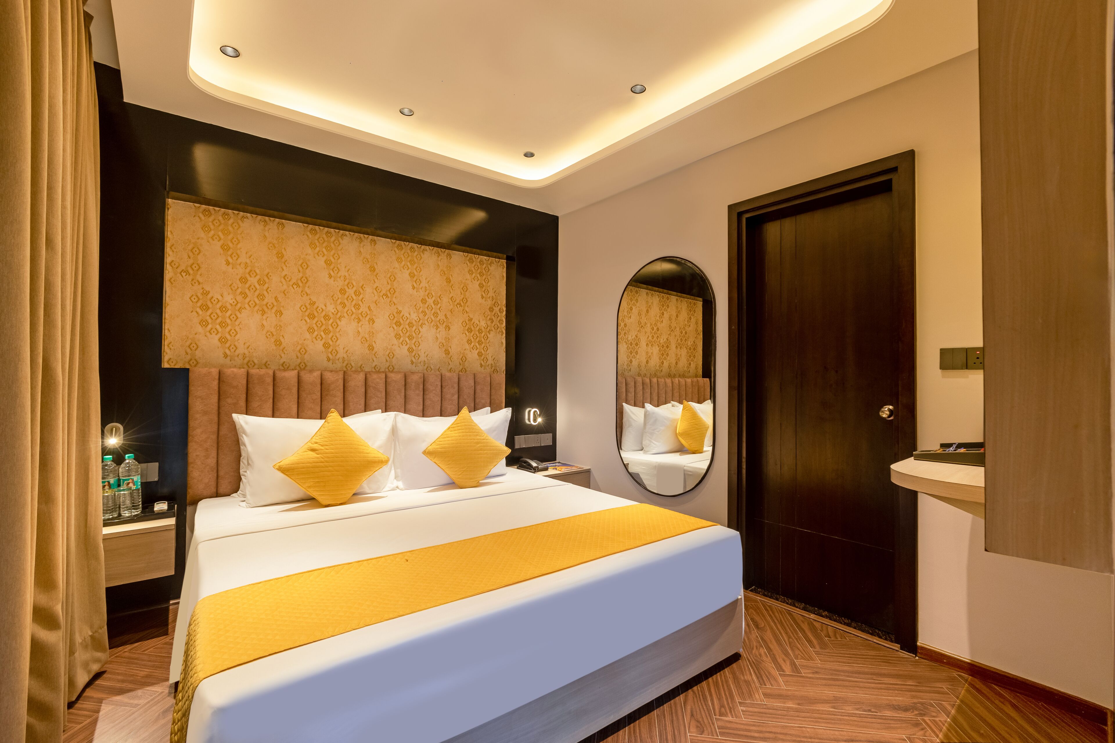 Una habitación de hotel con una cama grande, una mesita de noche con lámpara, un espejo y una puerta.