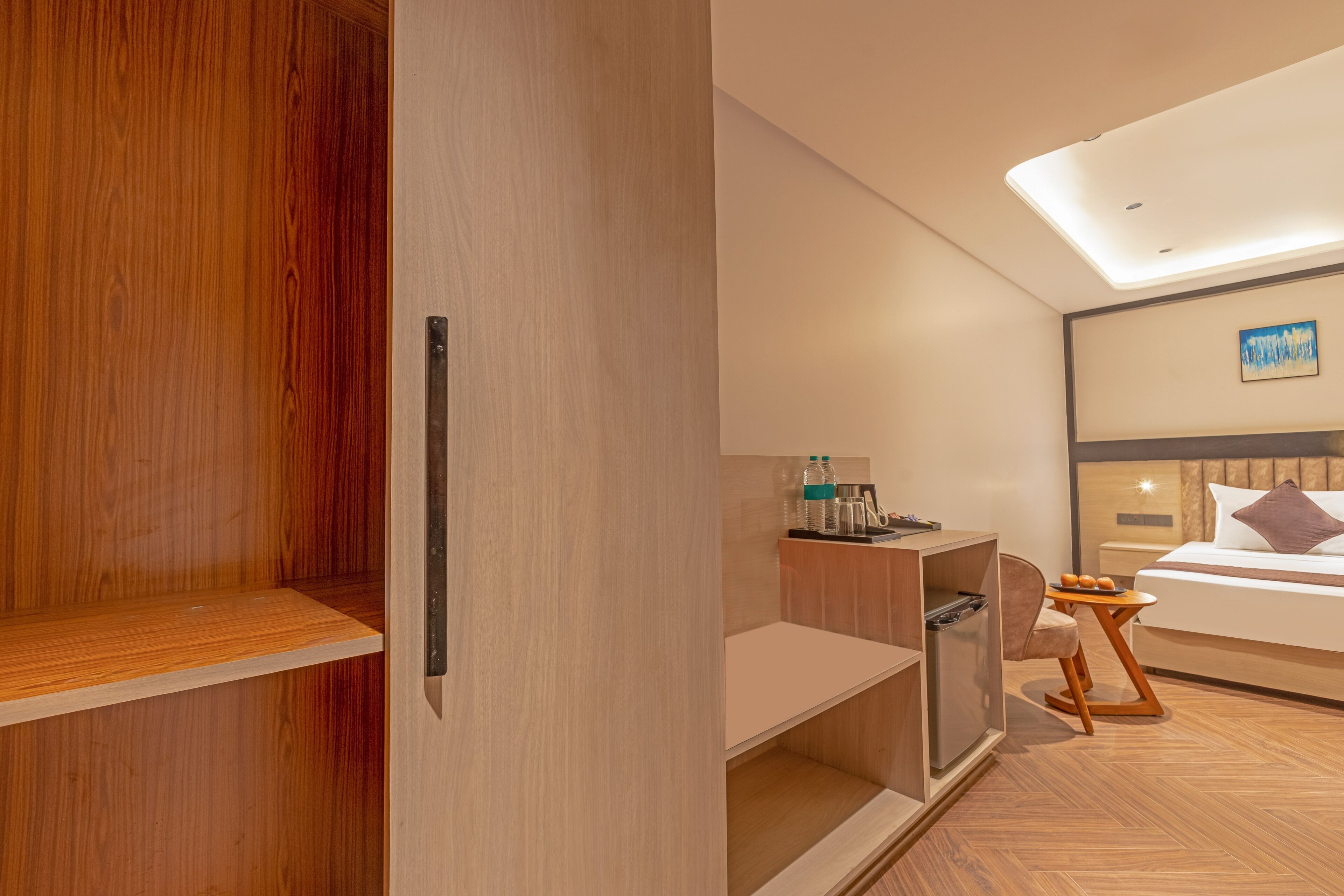 Una habitación de hotel moderna con un armario de madera, un escritorio con silla, una cama con cabecera y una pequeña mesa con otra silla.