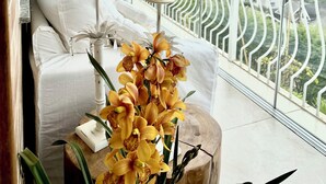Una habitación moderna con un ventanal grande, un sofá blanco, una mesita con una vela y un taburete de madera con flores.