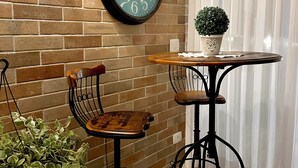 Una habitación con pared de ladrillo, una mesa redonda con planta en maceta, una silla y un reloj en la pared.