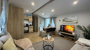Un salon moderne avec un téléviseur, un canapé et un coin repas, la cuisine étant visible au fond.