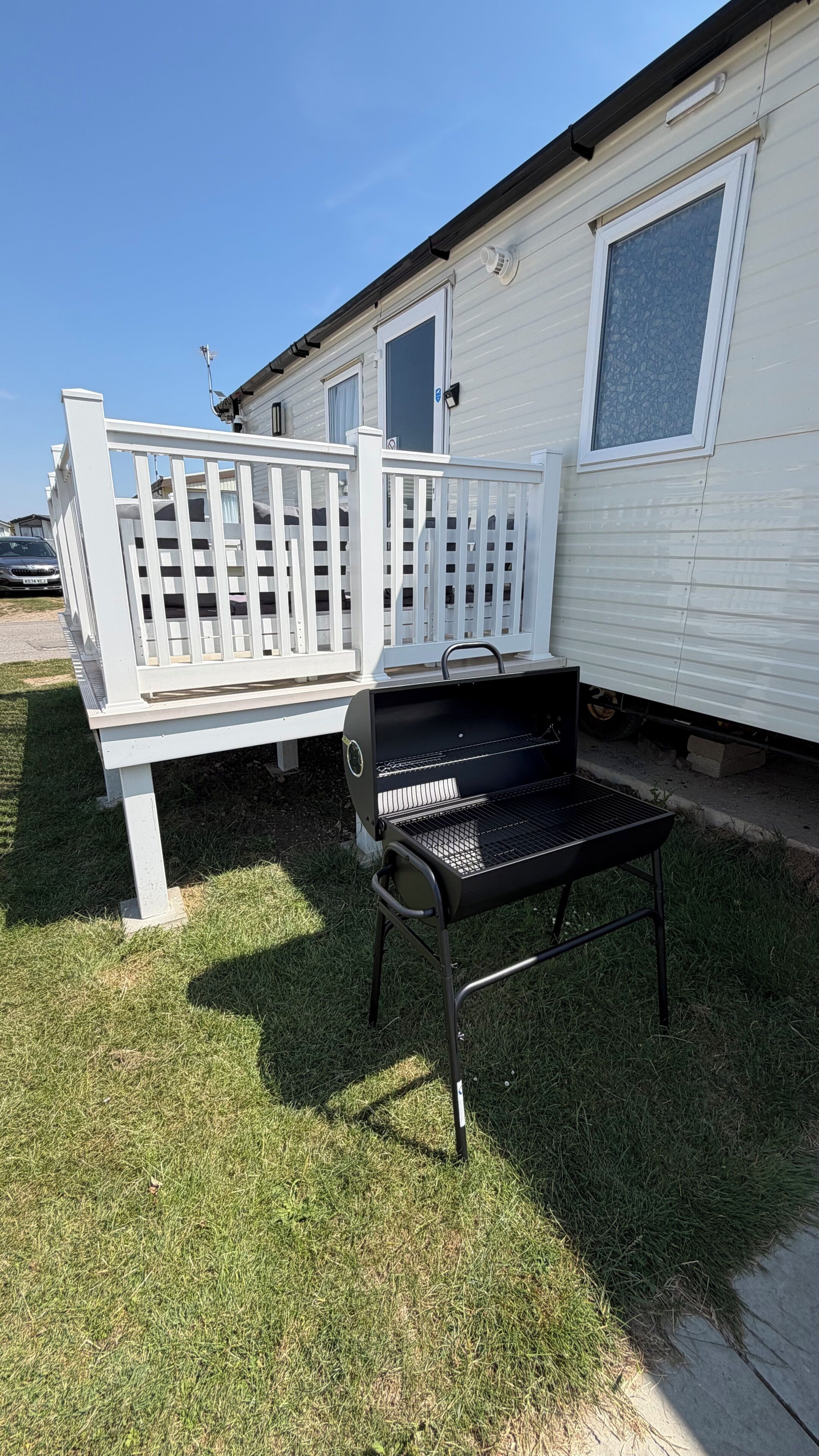 En transportabel grill og en hvid terrasse foran en autocamper.