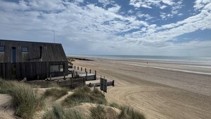 Et strandhus med træfacade, en sandstrand i baggrunden og en klar himmel.