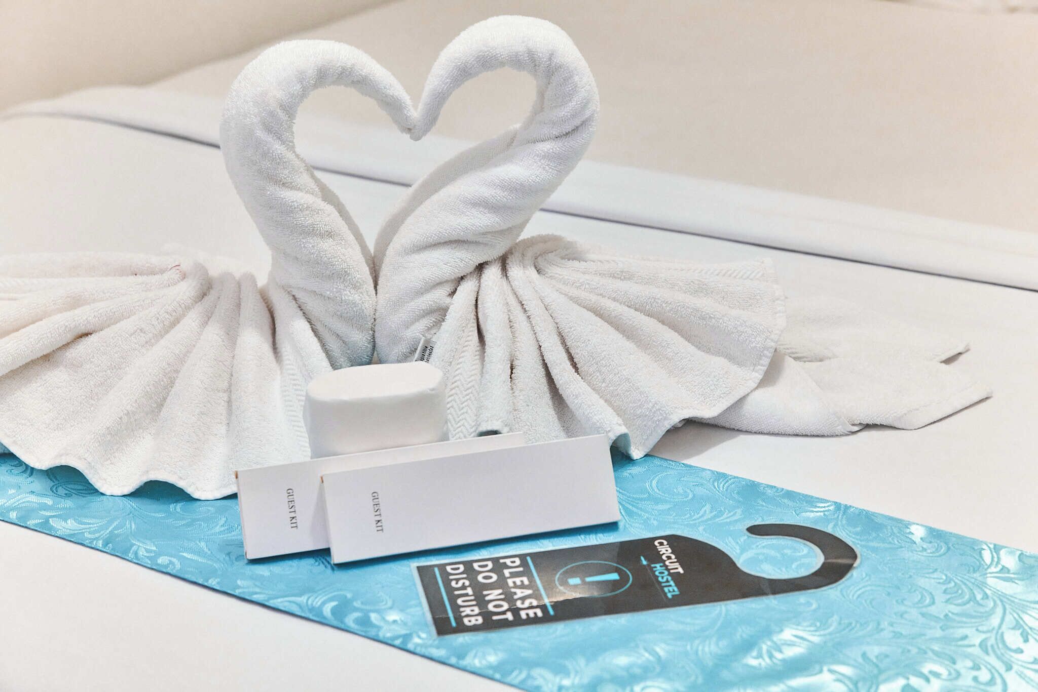 A hotel room with a towel art arrangement, a guest kit, and a sign indicating the room is part of the circuit hotel.