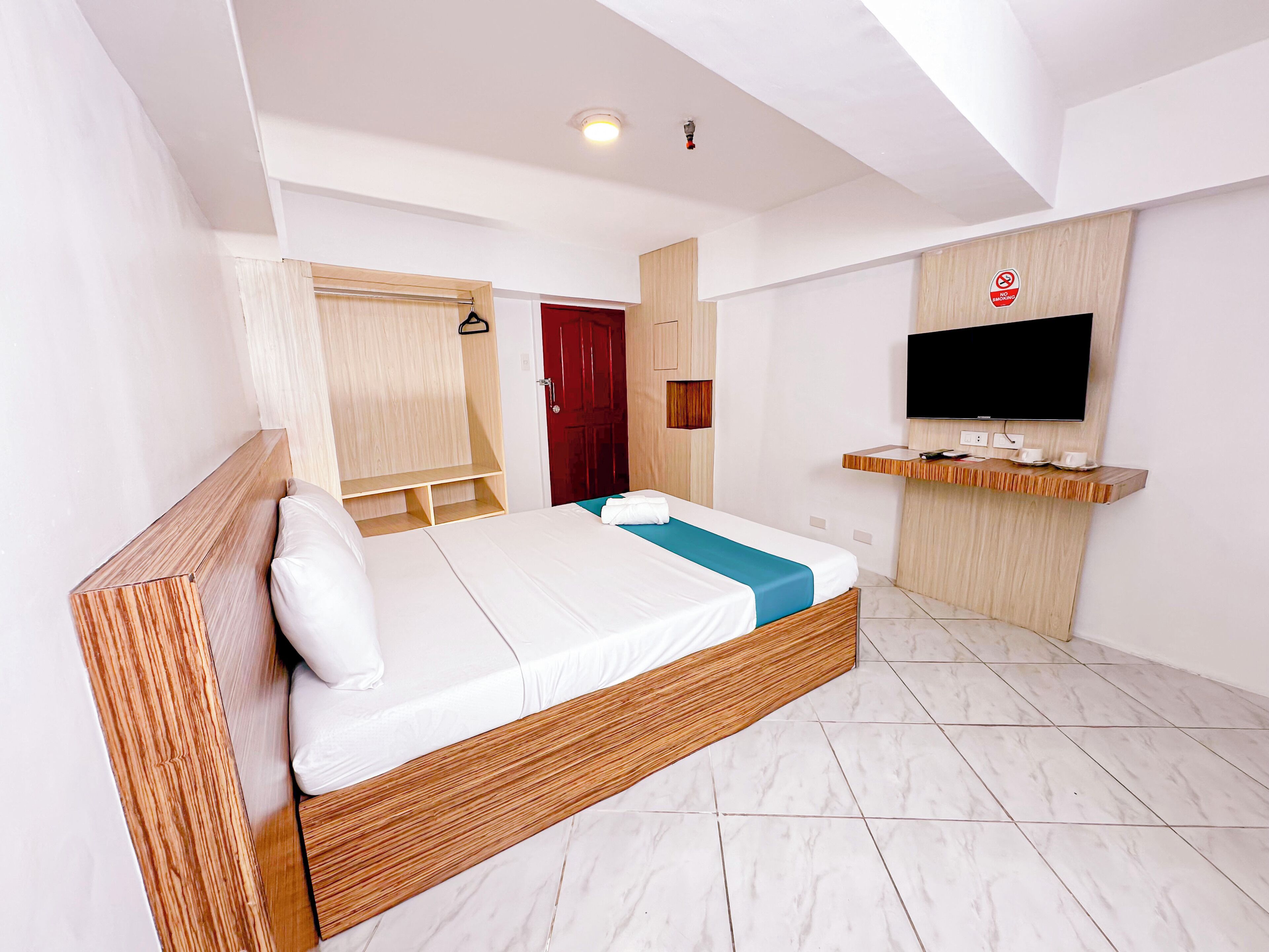A modern hotel room with a bed, wooden headboard, a TV mounted on the wall, and a red door.