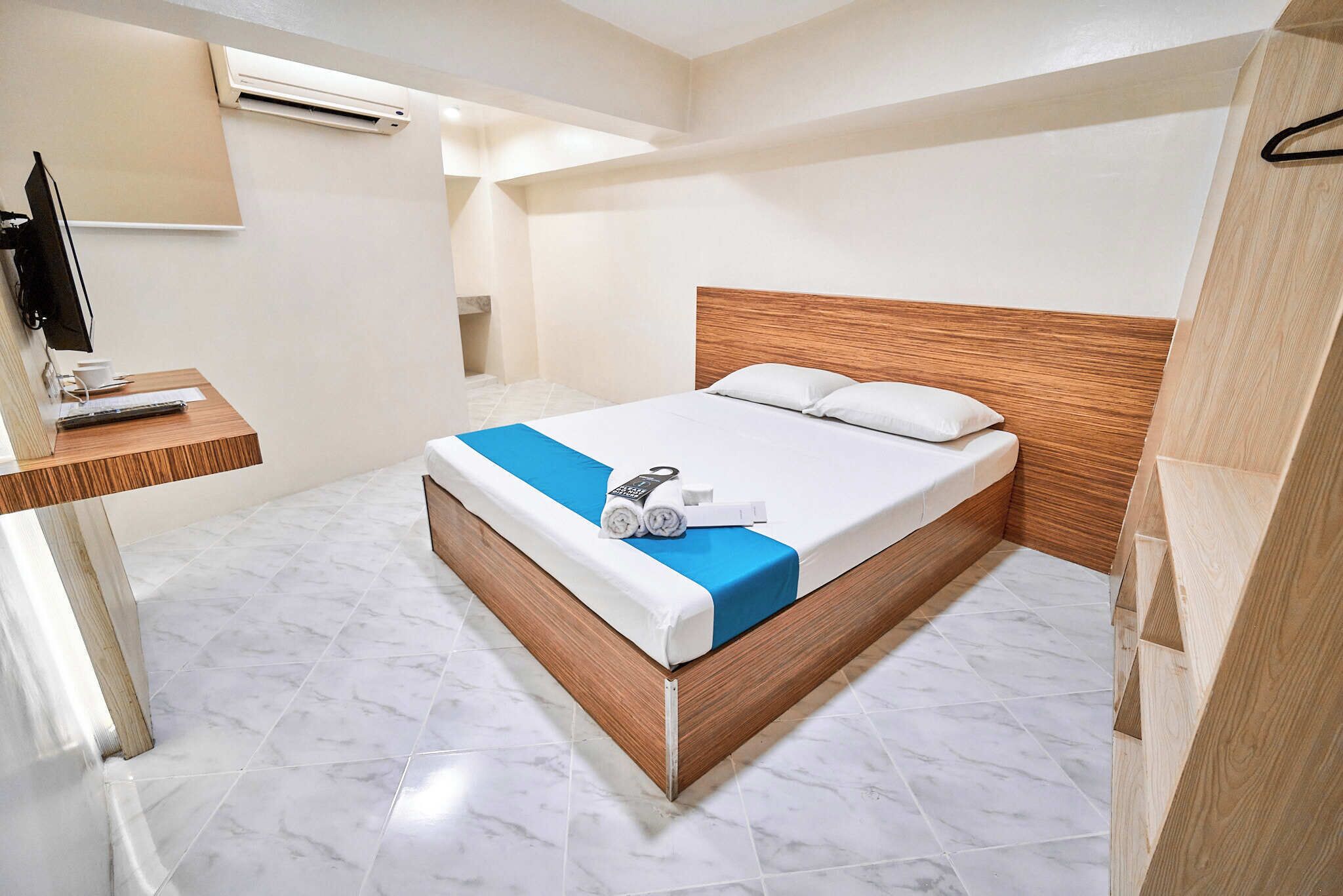 A hotel room with a wooden bed, a desk with a computer, and a bathroom with a shower.