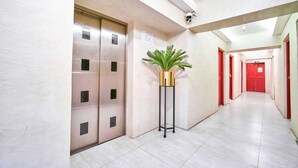 A hallway with an elevator, a potted plant, and red doors. - Circuit Hostel Makati (Makati)