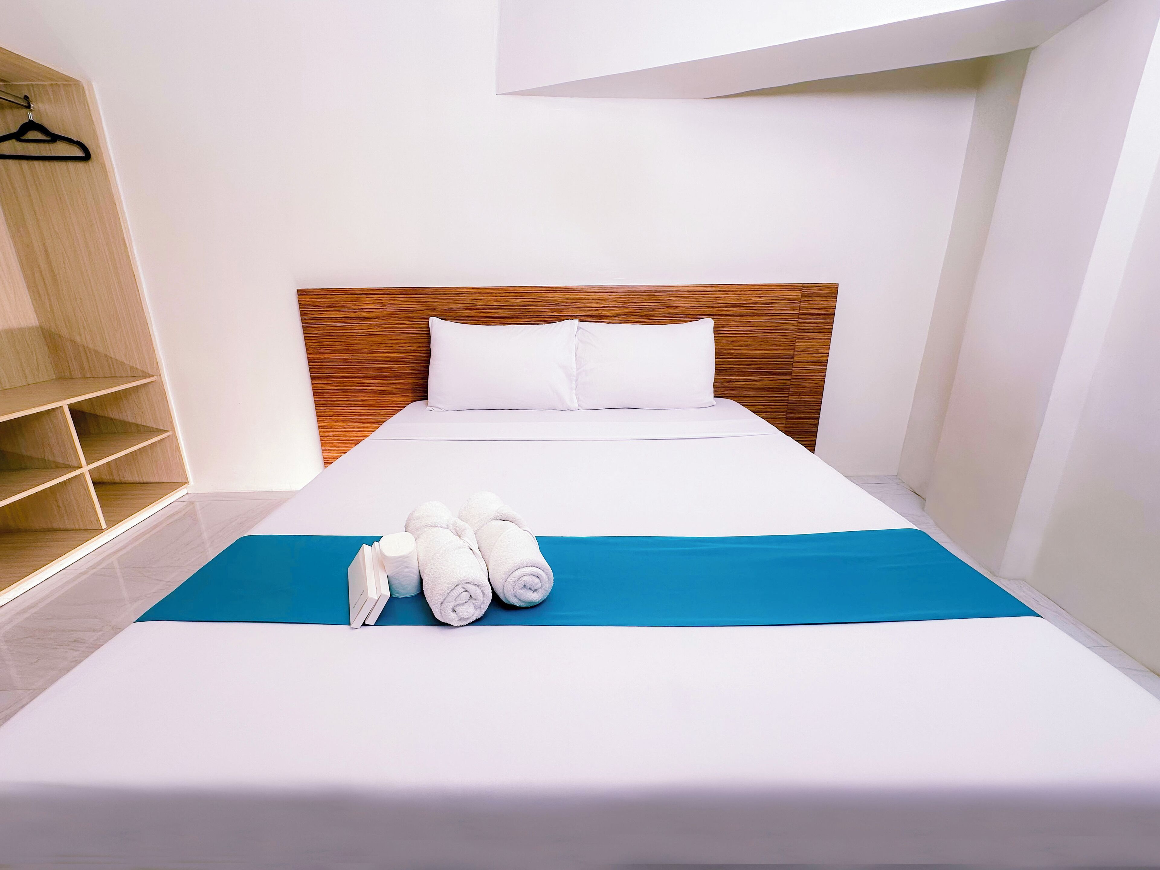 Una cama bien hecha con sábanas blancas y un toque de azul, un cabecero de madera y un almohadón blanco.