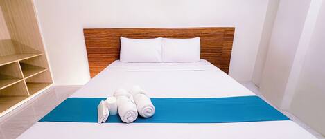 Una cama bien hecha con sábanas blancas y un toque de azul, un cabecero de madera y un almohadón blanco.