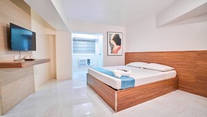 A modern hotel room with a wooden bed, a flat-screen TV mounted on the wall, and a large window offering a view of the sky. - Circuit Hostel Makati (Makati)