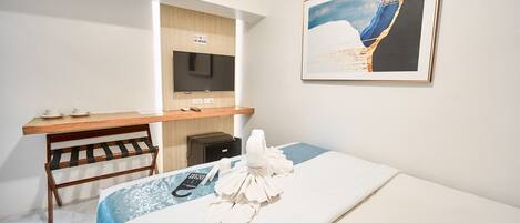 A hotel room with a bed, a desk with a chair, a TV, and a framed picture on the wall.