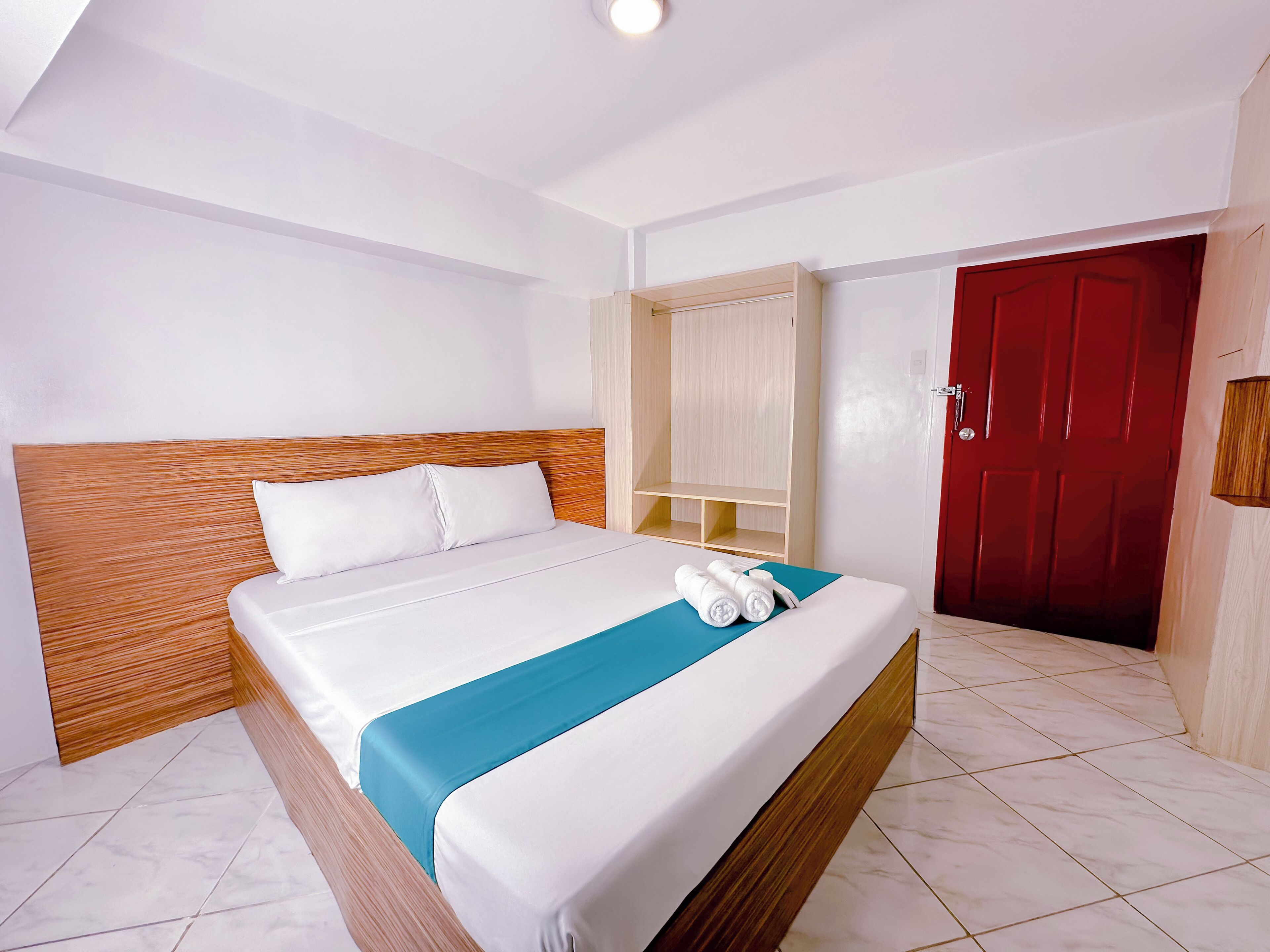 A hotel room with a bed, a wooden headboard, a red door, and a wardrobe.