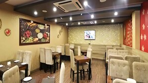 A restaurant with booths and tables, a ceiling with recessed lighting, and a wall-mounted TV. - Hotel Royal Castle Lucknow (Lucknow)