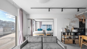 Una habitación de hotel moderna con un ventanal grande, un sofá, un escritorio y un kitchenette.