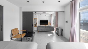 Una habitación de hotel moderna con sofá, televisión, mesa de comedor y un amplio ventanal.