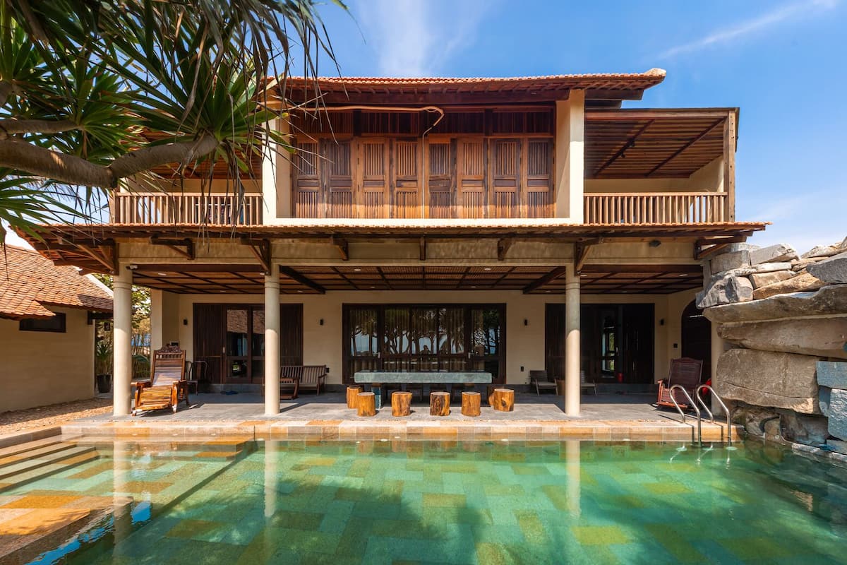 Un edificio de dos pisos con piscina, terraza de madera y zona de estar exterior.