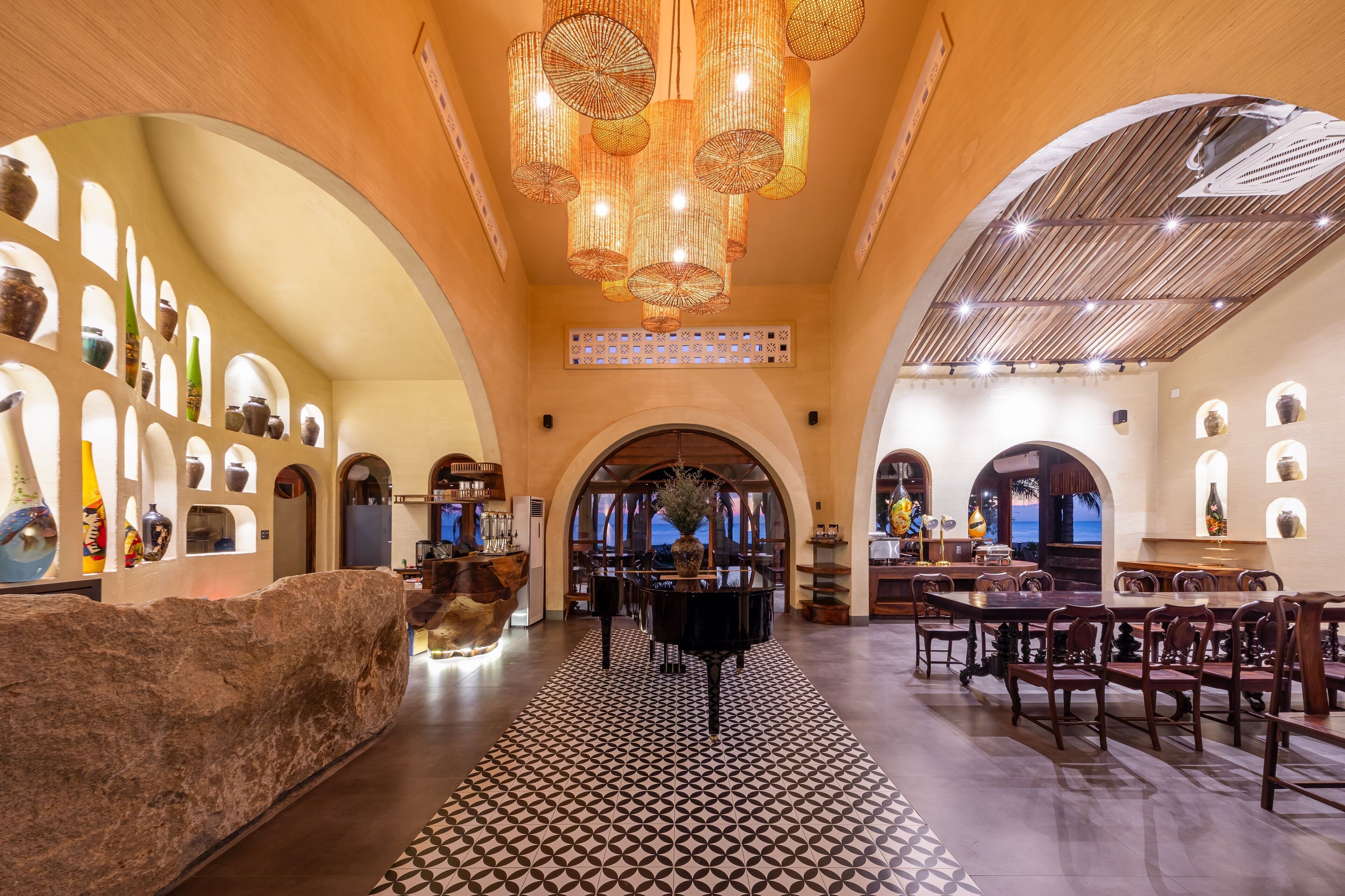 A spacious lobby with a grand piano, a patterned floor, and a large rock feature.