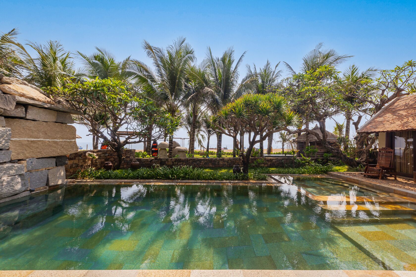 A pool with clear water, surrounded by palm trees and stone structures.