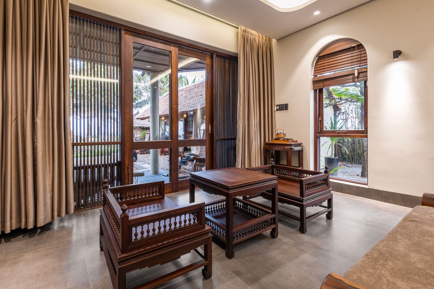 A room with a wooden table and chairs, a large window with curtains, and a view of the outside.