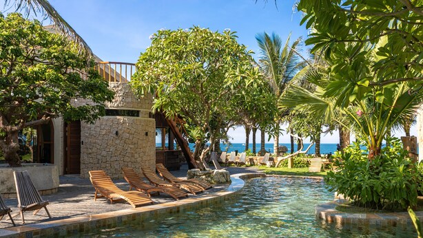A pool area with lounge chairs, a stone building, and tropical vegetation. - Sun Village Beach Resort (Hoa Hiep)