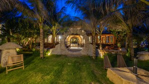 A tropical resort with a stone archway entrance, outdoor seating area, and palm trees. - Sun Village Beach Resort (Hoa Hiep)