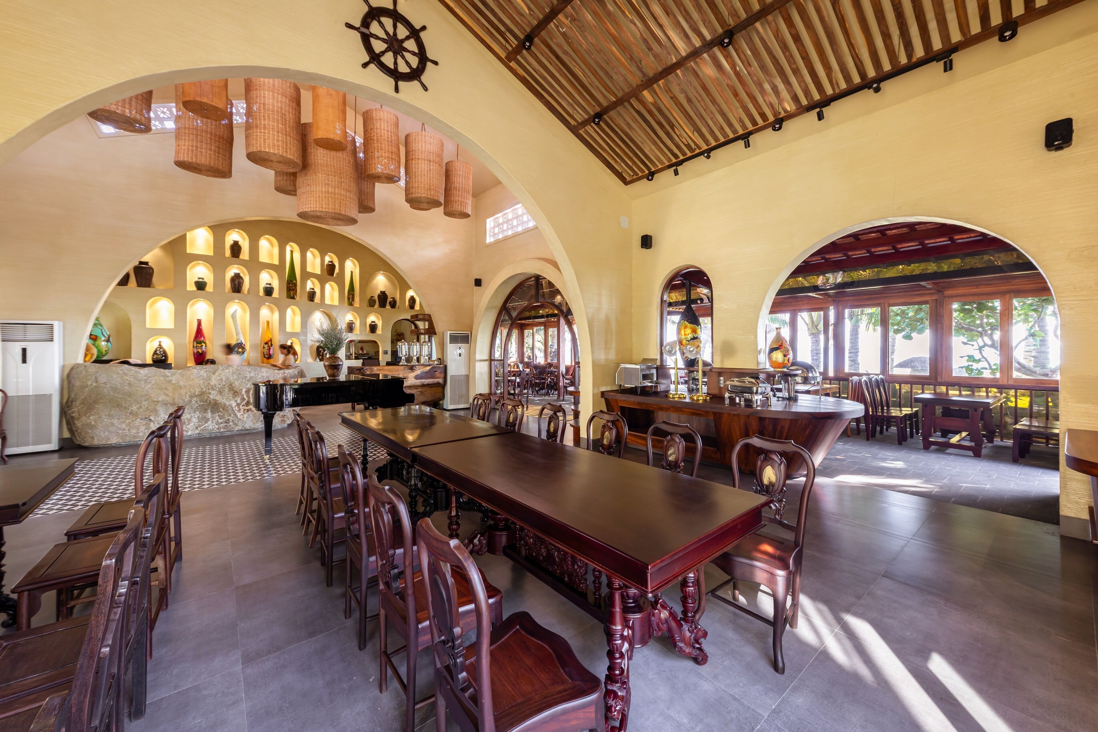 A spacious dining area with a long wooden table and chairs, a piano, and a wall of decorative vases.