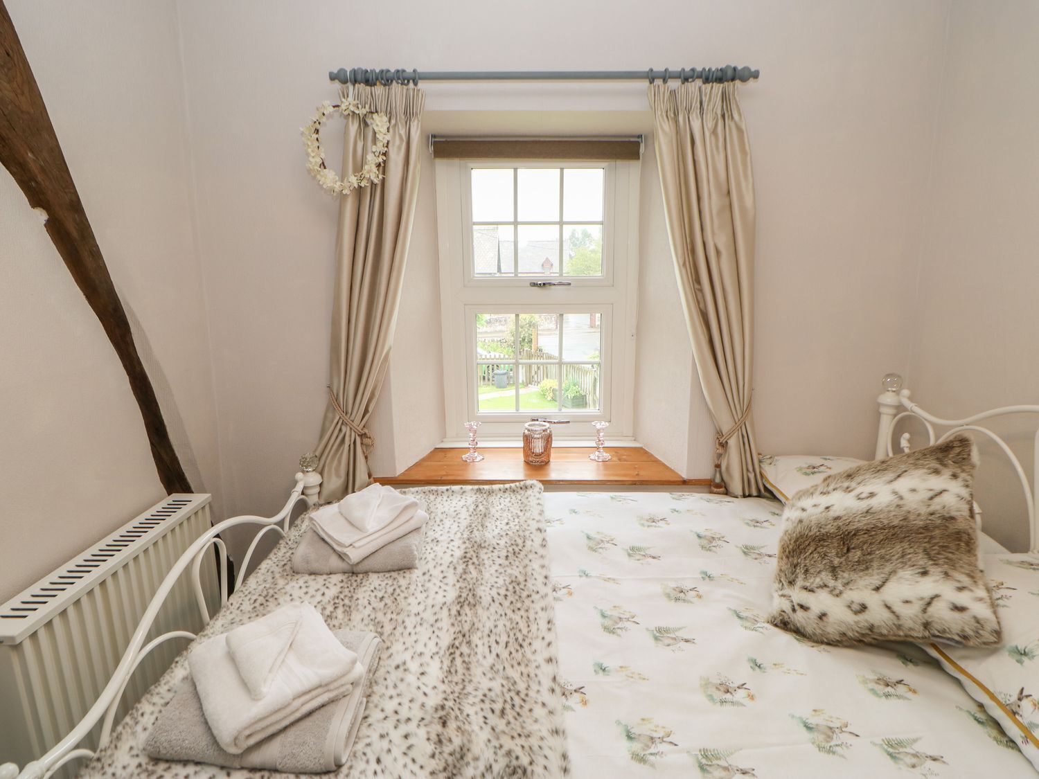 A bedroom with a bed, a window with curtains, a radiator, and a bedside table with a lamp and a glass jar.