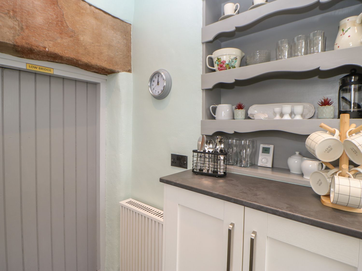 A kitchen with white cabinets, a grey countertop, and shelves holding various kitchenware.