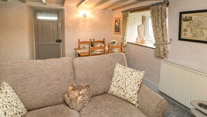 A cozy room with a wooden ceiling, a dining table set with plates and a bottle, a sofa with patterned cushions, and a radiator.