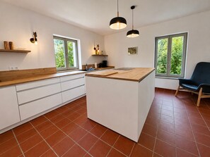 Une cuisine moderne dotée d’un îlot central, de meubles blancs et de grandes fenêtres.