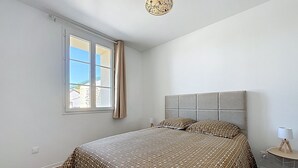 Un dormitorio con cama, una ventana con cortinas, una lámpara de noche y una mesita con lámpara.