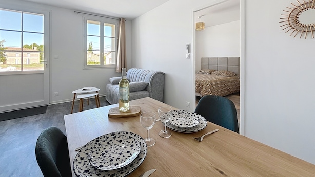 Un comedor con una mesa de madera dispuesta para dos personas, una botella de vino y un adorno en la pared.