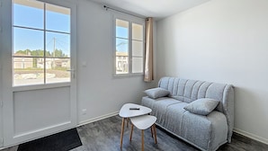Un salón moderno con un sofá gris, una mesita blanca y dos ventanas con cortinas.