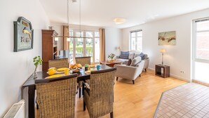A dining area with wicker chairs, a table set with yellow plates, and a view of the outdoors through large windows.