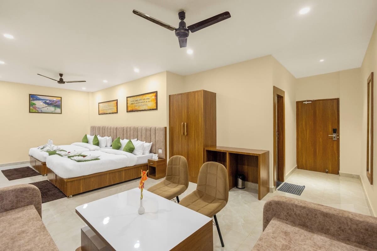 A hotel room with a bed, two chairs, a desk, a coffee machine, and a ceiling fan.