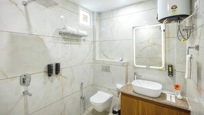 A modern bathroom with a white marble floor, a built-in toilet, a sink with a mirror, a towel rack, and a shower with a handheld showerhead. - Hotel Veda Inn By Blue Lotus (Rishikesh)