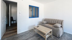 A modern living room with a grey sofa, a wooden coffee table, and a blue-framed window.