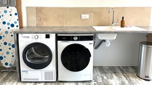 A laundry area with two front-loading washing machines, a sink, and a trash can.