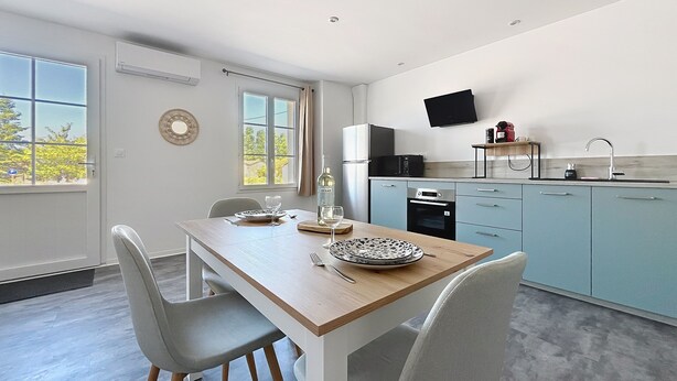 A modern kitchen with a dining area, featuring a wooden table, grey chairs, and a flat-screen TV mounted on the wall.