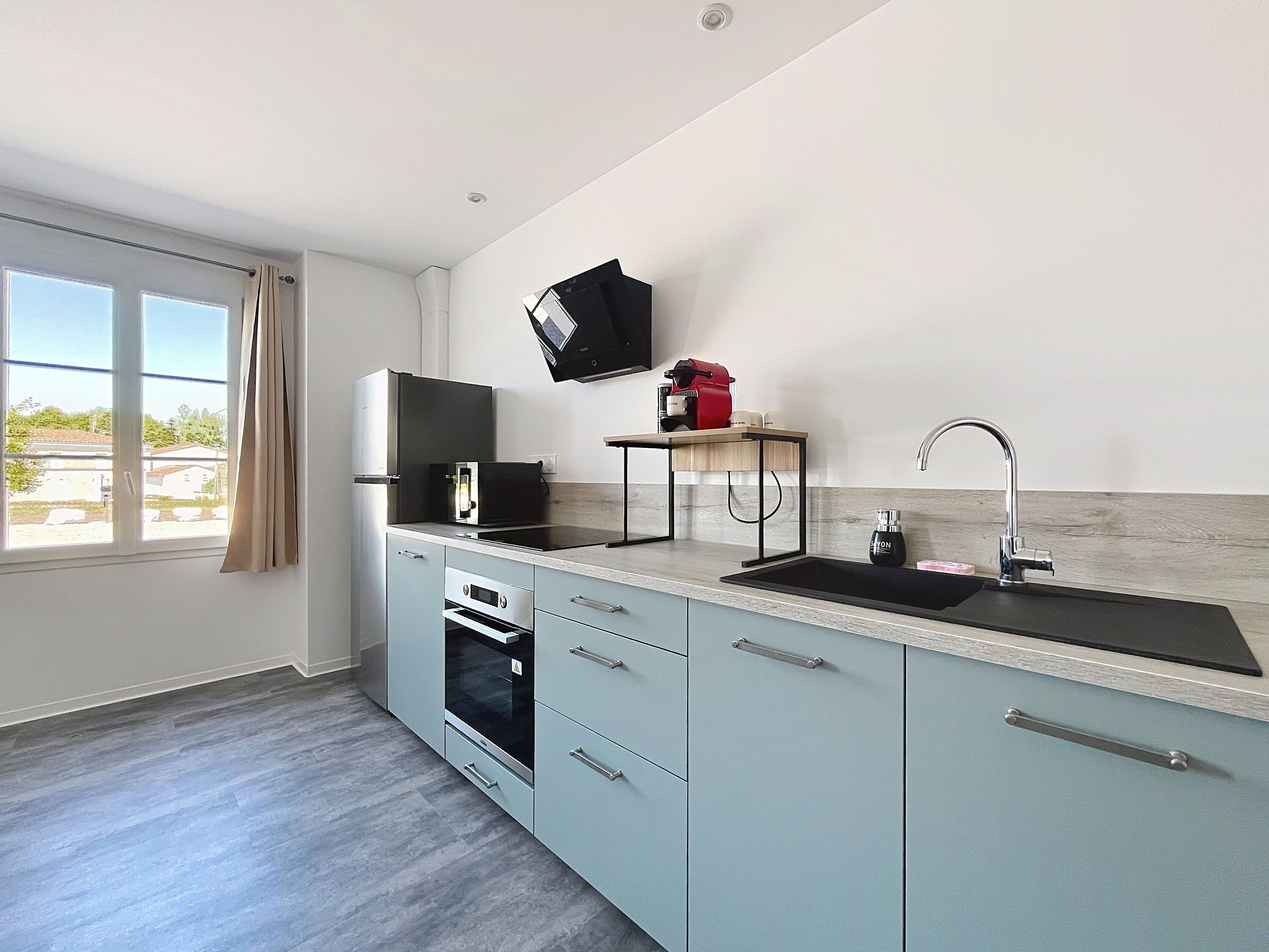 A modern kitchen with a built-in oven, a sink, and a flat-screen TV mounted on the wall.