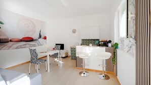 Eine moderne Küche mit Kochinsel, Barhocker, einem Essbereich mit weißem Tisch und gemusterten Stühlen sowie einem Wohnbereich mit Sofa und dekorativen Wandbildern.