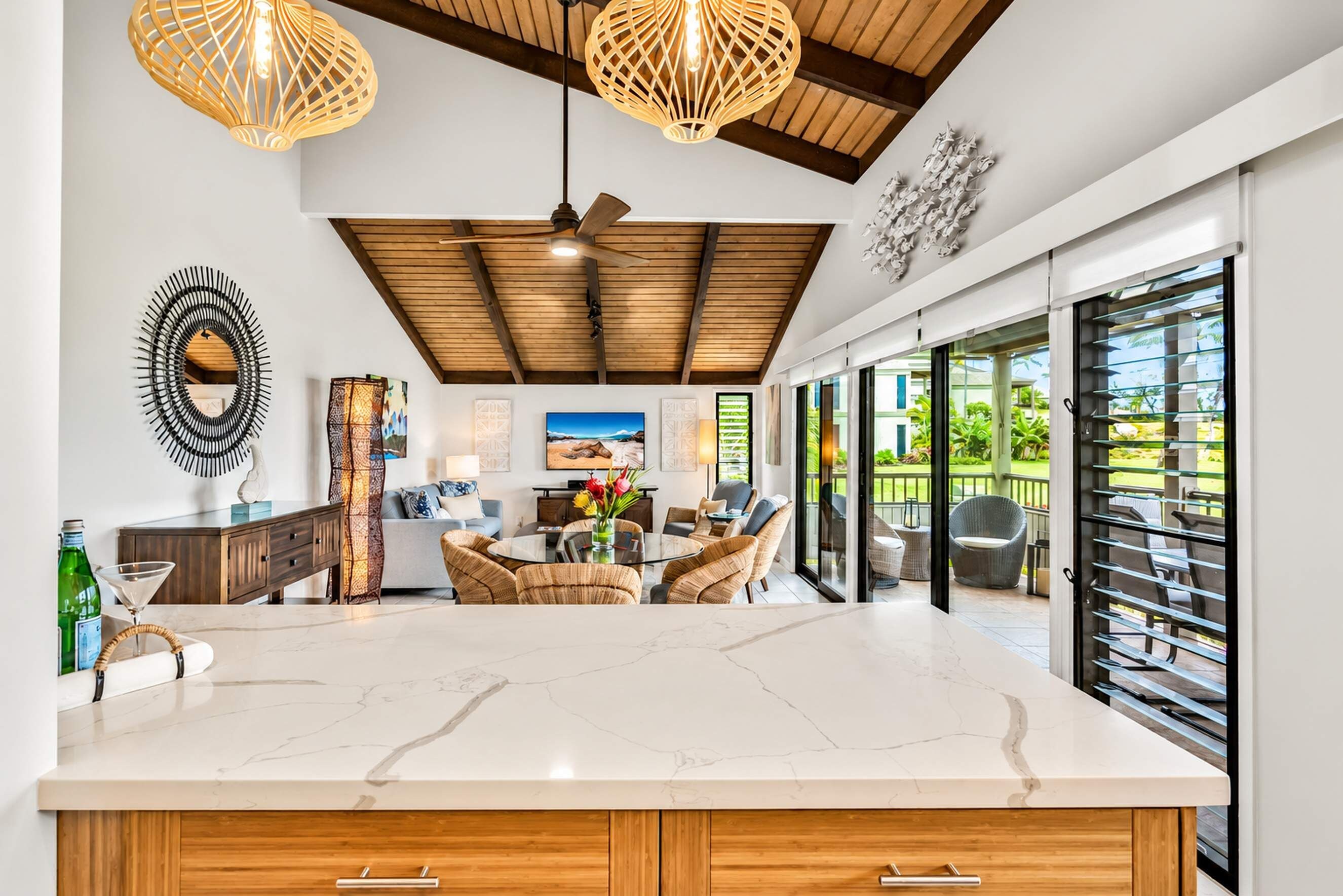 A modern kitchen with a marble countertop, wooden cabinets, and a dining area with wicker furniture.