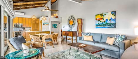 A modern living room with a sofa, chairs, a coffee table, and a dining area with a kitchen in the background.