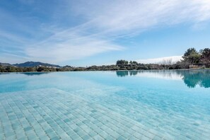 A clear blue pool with a tiled edge, surrounded by a natural landscape with trees and distant hills. - Ground Floor Room with Shared Pool, Wi-Fi, and Air Conditioning (Artá)