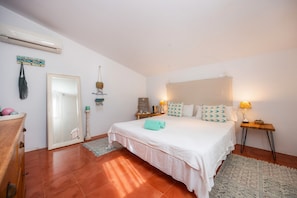 A bedroom with a bed, bedside tables, a mirror, a hanging bag, and a wall-mounted air conditioner. - Ground Floor Room with Shared Pool, Wi-Fi, and Air Conditioning (Artá)