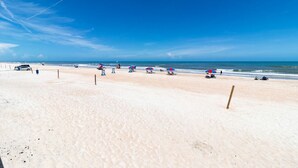 A beach with a clear sky, a sandy shore, and a few umbrellas and beach chairs. - Azure Tides Oceanfront (Daytona Beach)