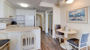 A modern kitchen with white cabinets, a central island, and a dining area with two chairs and a small table. - Azure Tides Oceanfront (Daytona Beach)