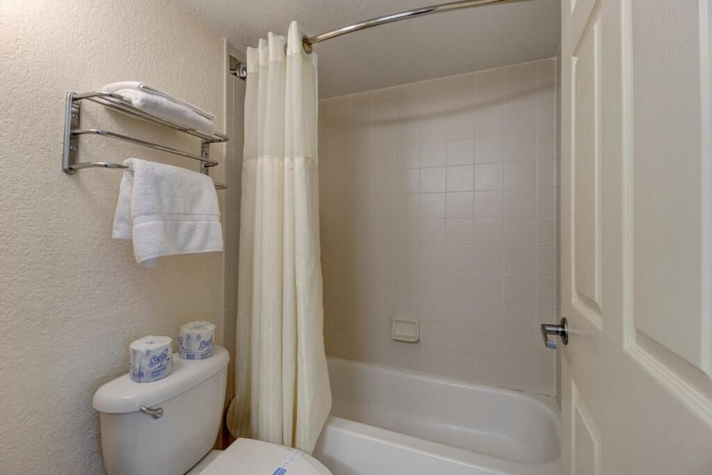 A bathroom with a toilet, two rolls of toilet paper, a towel rack with two towels, and a shower curtain.