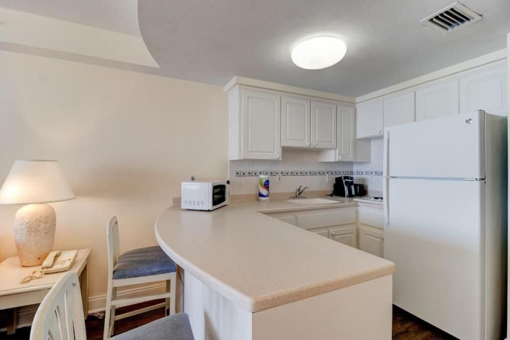 Cocina compacta con armarios blancos, microondas, cafetera y refrigerador.