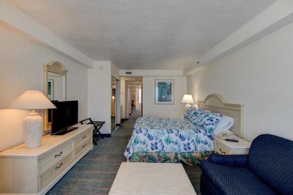 A hotel room with a bed, a TV, a desk, a chair, a lamp, and a sofa.